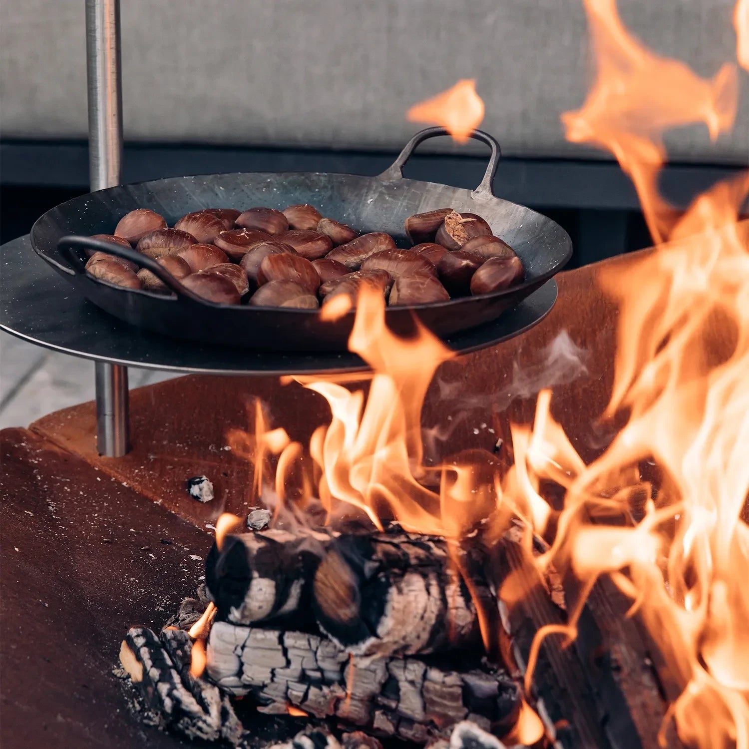 Höfats TRIPLE 120 Fire Pit in Corten Steel with burning logs, placed on a white surface.